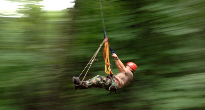 A person wearing safety gear is secured by ropes. They appear to be moving on a zip line through trees. 